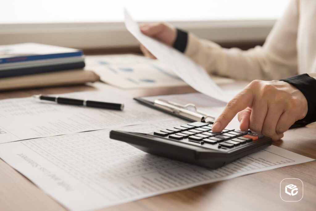 Mão de contabilidade segurando uma calculadora em cima de papéis e documentos