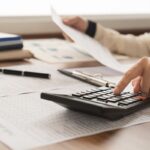 Mão de contabilidade segurando uma calculadora em cima de papéis e documentos