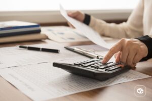 Mão de contabilidade segurando uma calculadora em cima de papéis e documentos